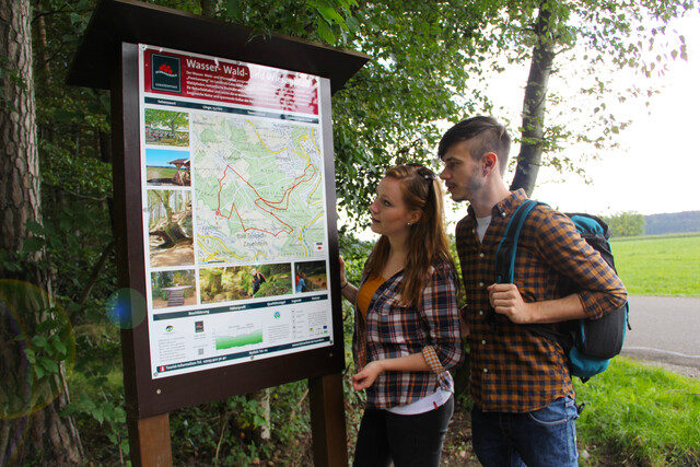 Zwei Wanderer stehen vor der Wandertafel des Premiumweges Wasser-, Wald- und Wiesenpfad